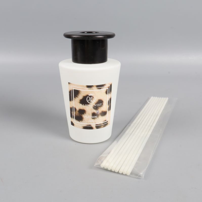 Vit flaska med leopardetikett och doftstickor bredvid