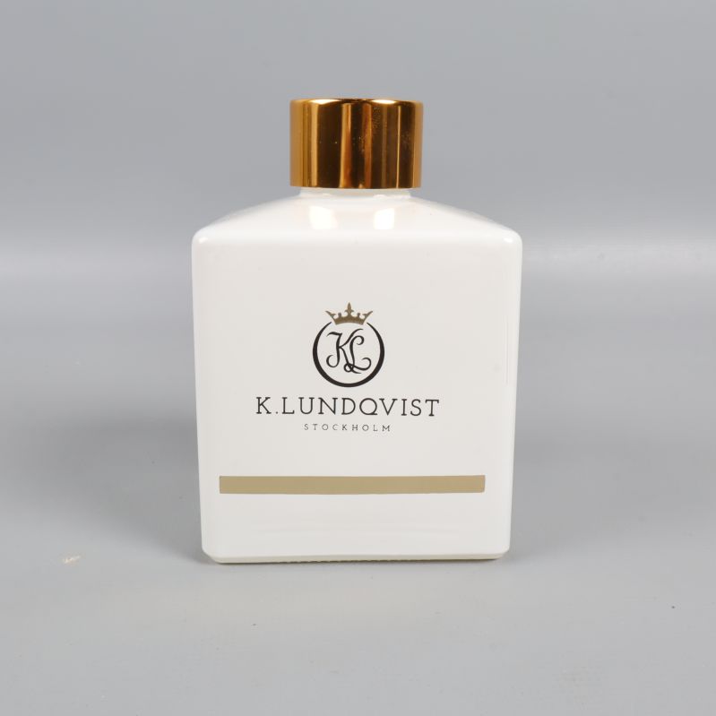 Framsidan av vit doftpinnflaska med guldlock och logotyp