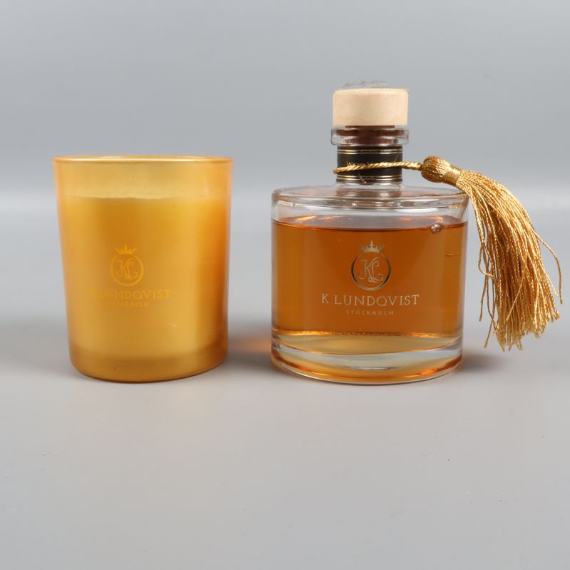 Doftljus i guld samt rund doftflaska nära varandra