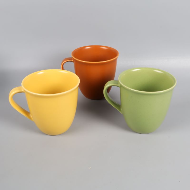 Närbild på tre muggar i gul, grön och orange