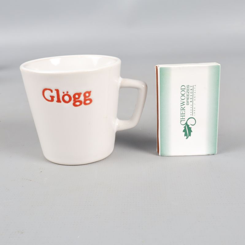 En vit glöggmugg bredvid tändsticksask för storleksjämförelse