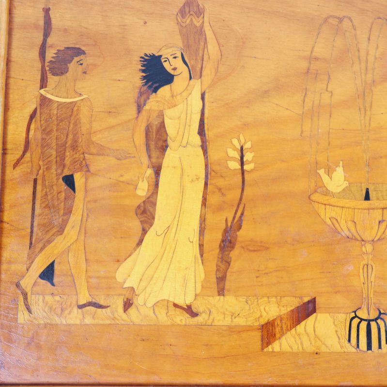 Närbild på brickans motiv med två personer och fontän