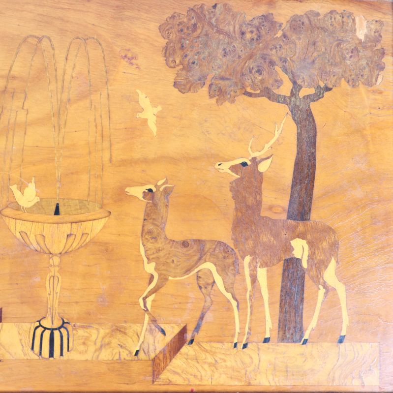 Närbild på brickans motiv med hjort, träd och fontän