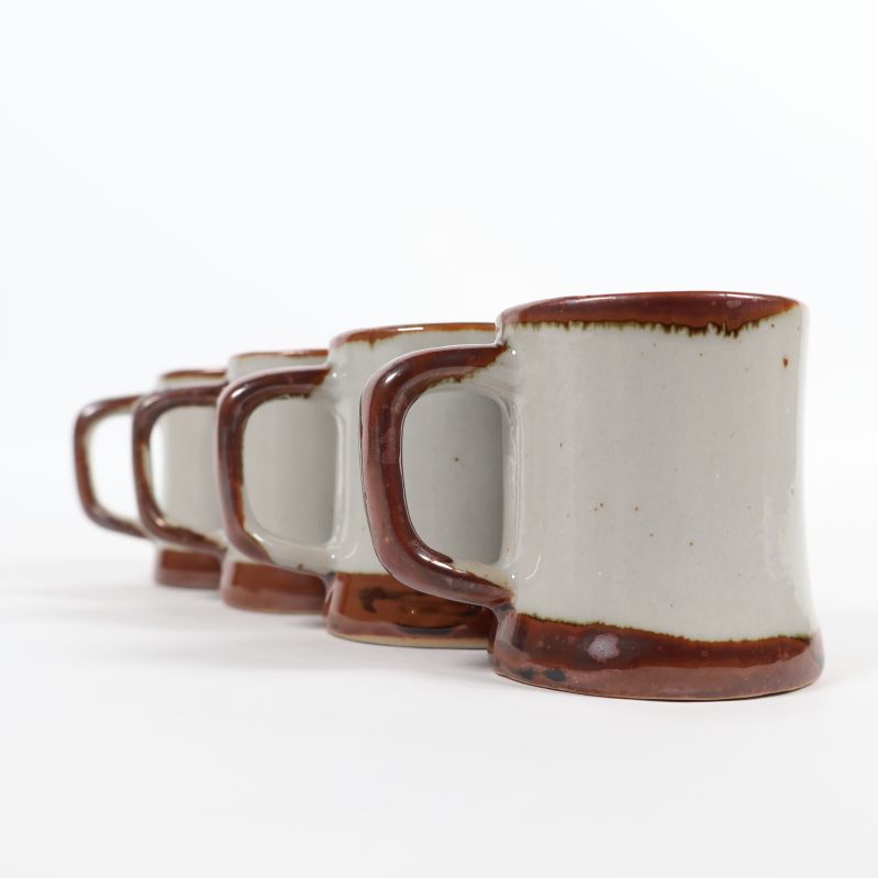 Sido vy av fyra små keramikmuggar med bruna detaljer
