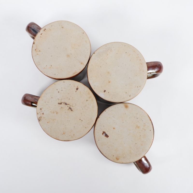 Botten av fyra små keramikmuggar i beige nyans