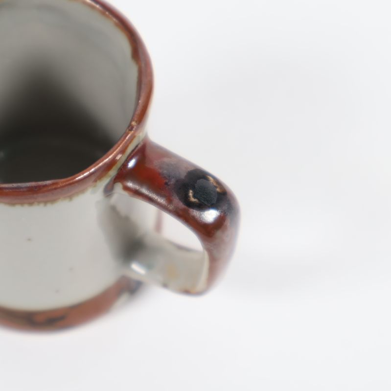 Närbild av kopp med dekorativ brunsvart prick på handtaget