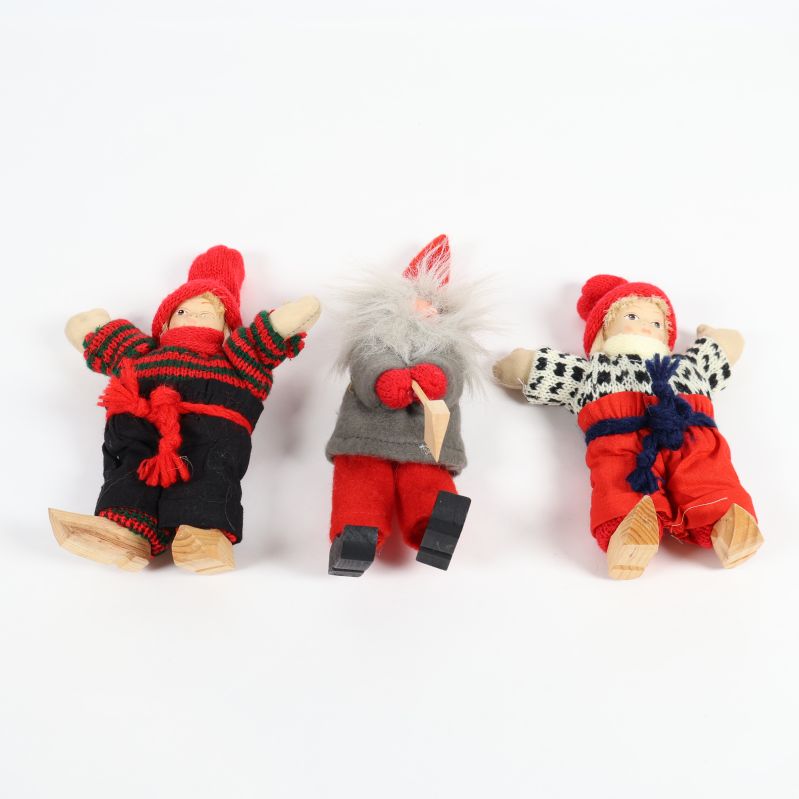 Tre julfigurer i färgglada kläder liggande på vitt underlag