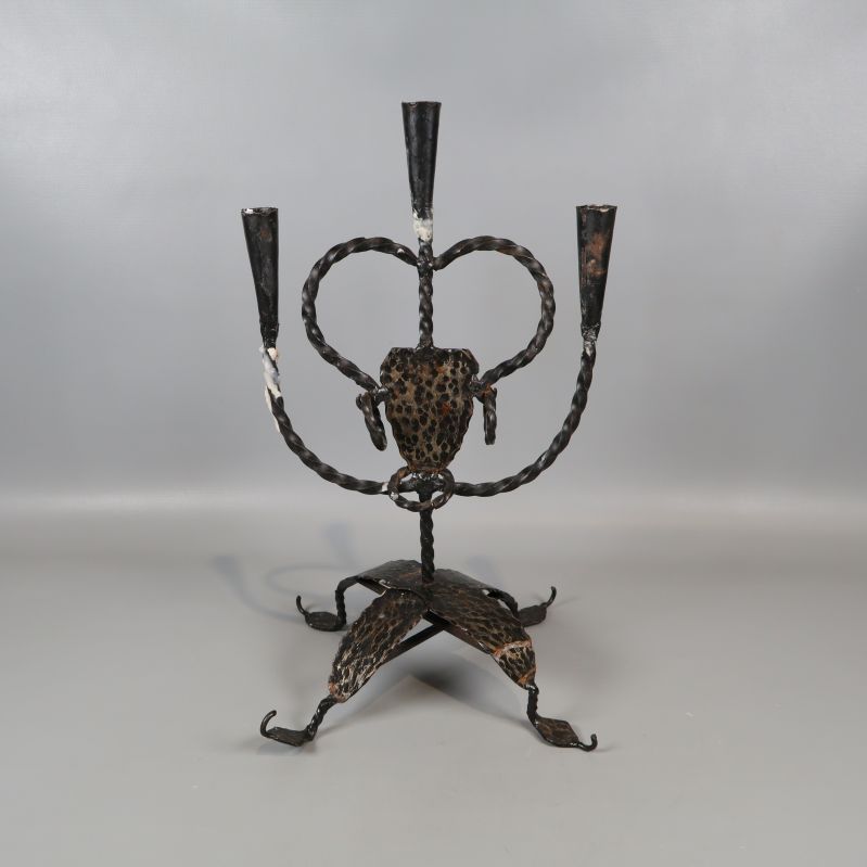 Tredelad smidesljusstake med svart patina på grå bakgrund