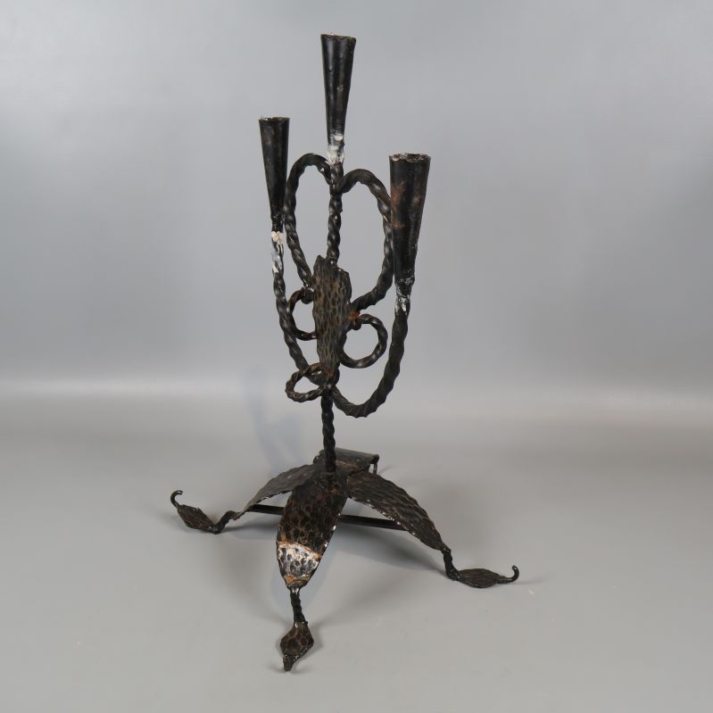 Smidesljusstake sedd snett bakifrån mot grå bakgrund