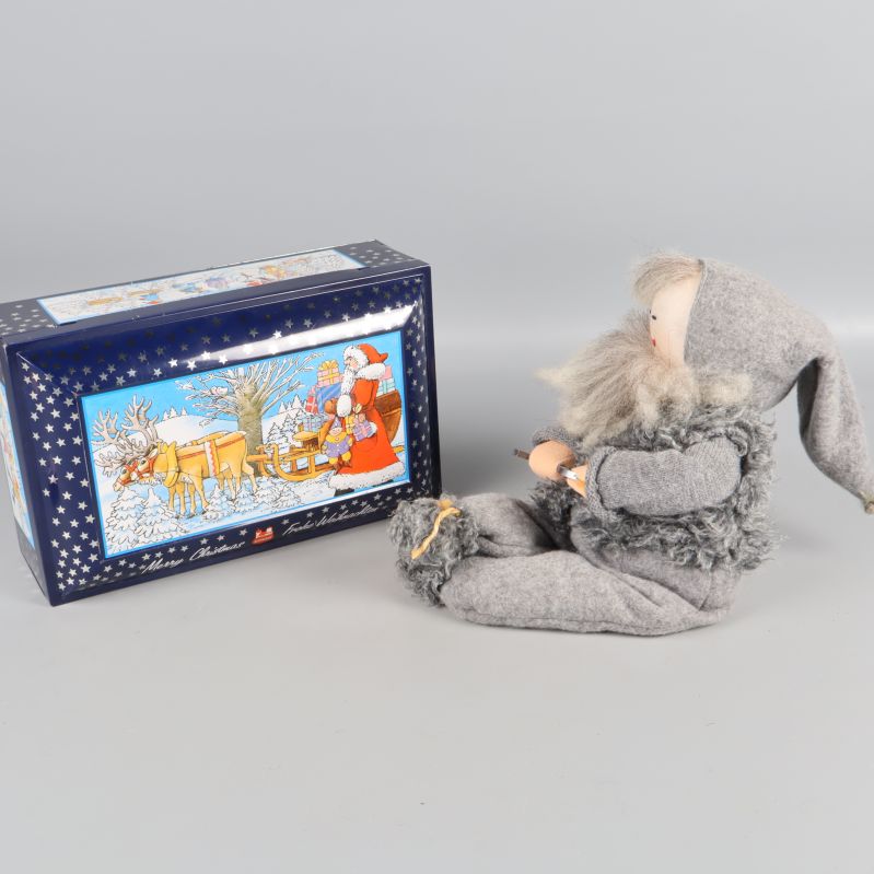 Tomtefigur sittande bredvid julburk med vintermotiv