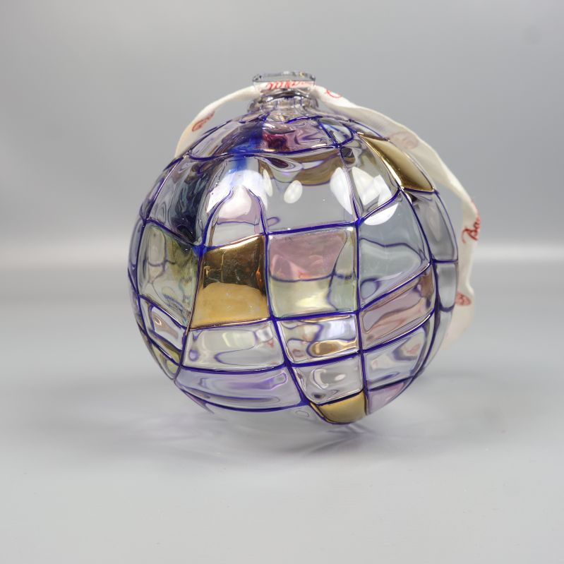 Glaskula med lila linjer och guldfärgade inslag syns framifrån
