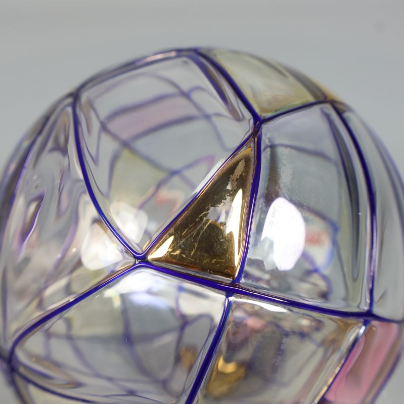 Närbild på glaskula med lila linjer och guldfärgade trianglar