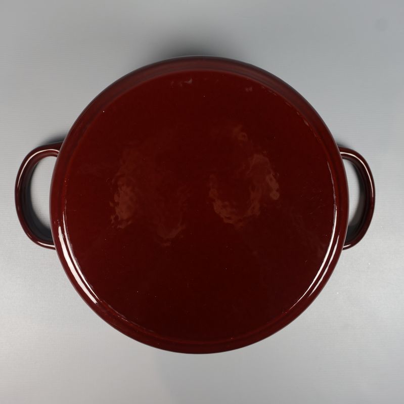 Undersida av mörkröd gryta med två handtag synliga