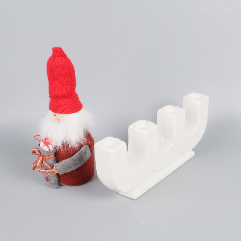 Tomtefigur intill vit adventsljusstake från sidan