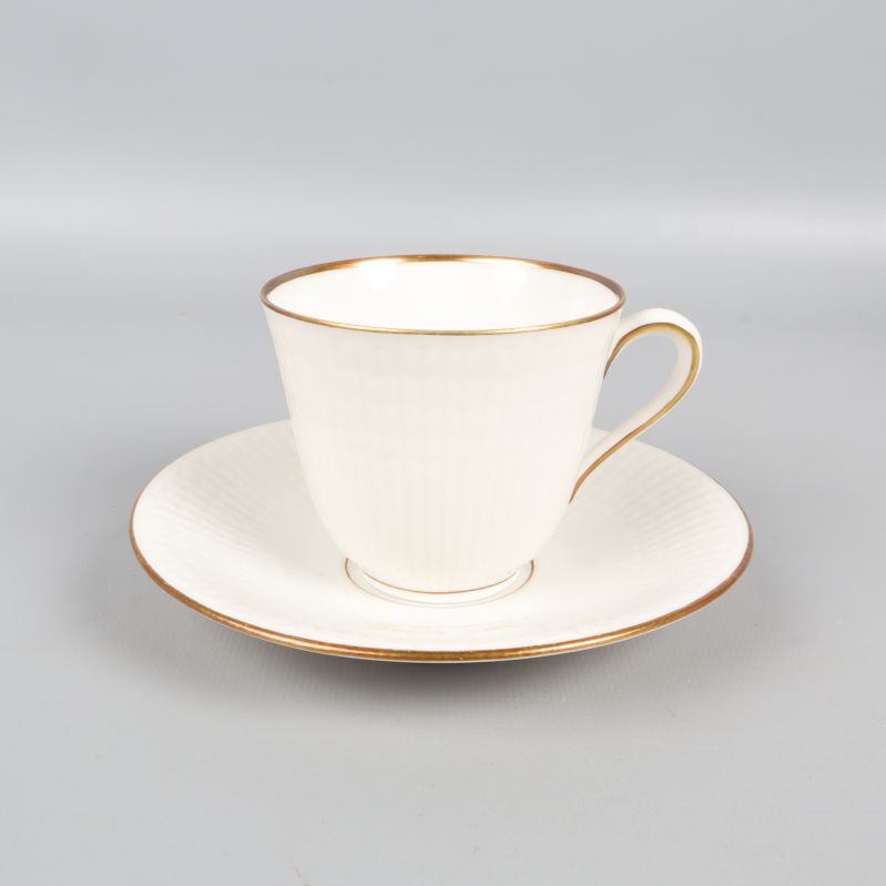 Närbild på kopp och fat i vitt porslin med guldkant