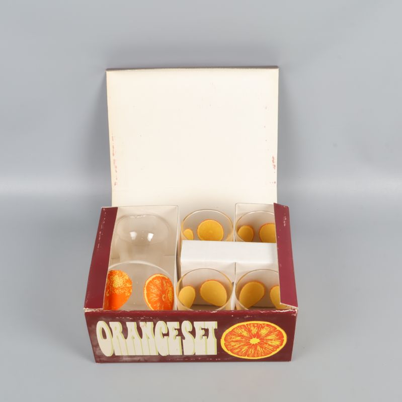 Öppen kartong med karaff och fyra apelsinglas i fack