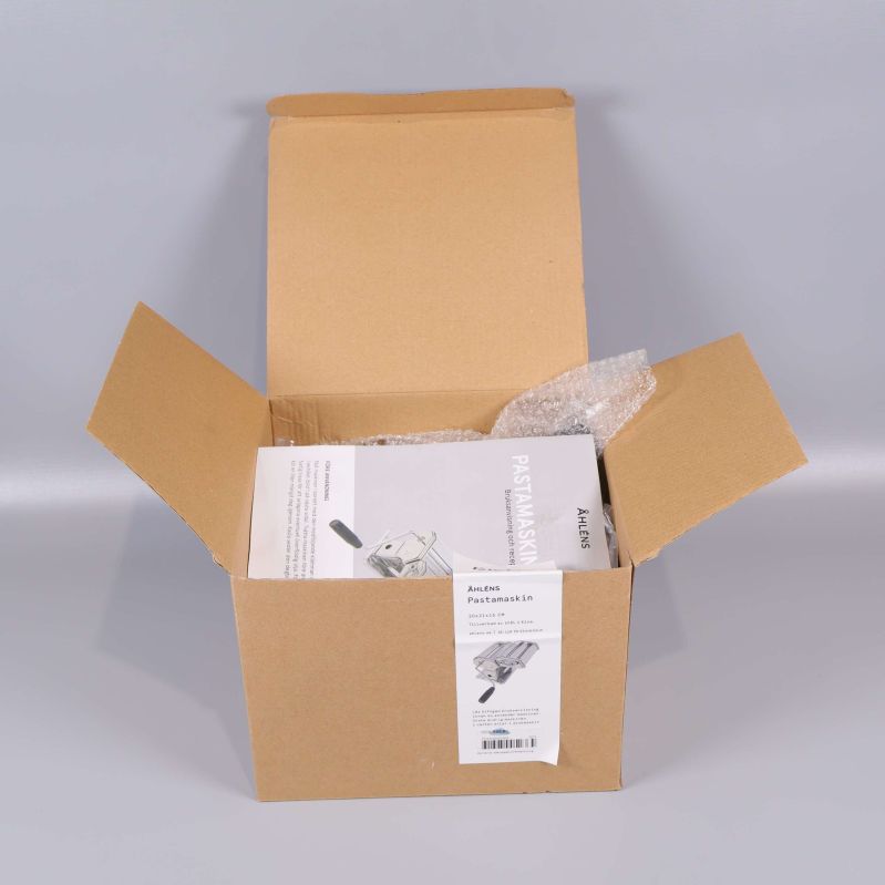 Öppen kartong med pastamaskinens manual ovanpå