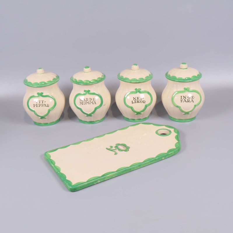 Fyra kryddburkar och en rektangulär skärbräda med grön kant