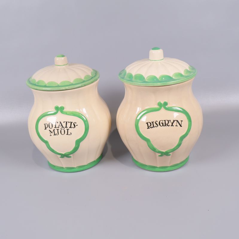 Två krämfärgade burkar med grön kant och lock