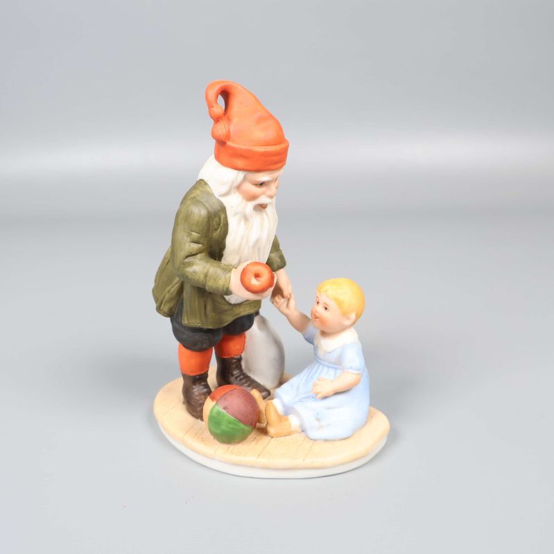 Tomtefigur står bredvid sittande barn på rund bas