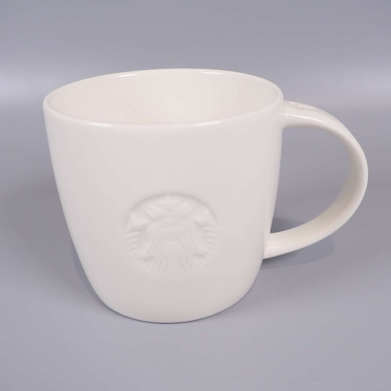 Närbild på vit mugg med reliefmönstrad Starbucks-logotyp