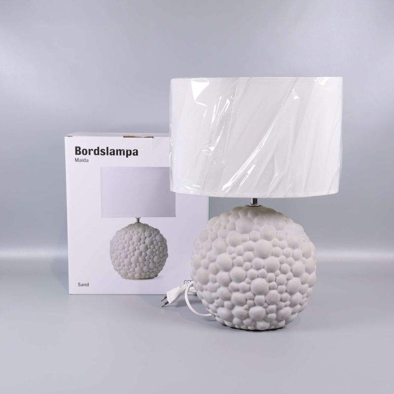 Vit bordslampa med bubblig bas framför originalförpackning