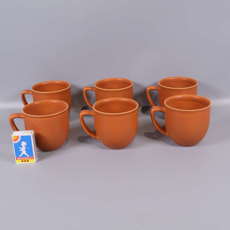 Sex orangea kaffekoppar placerade bredvid tändsticksask