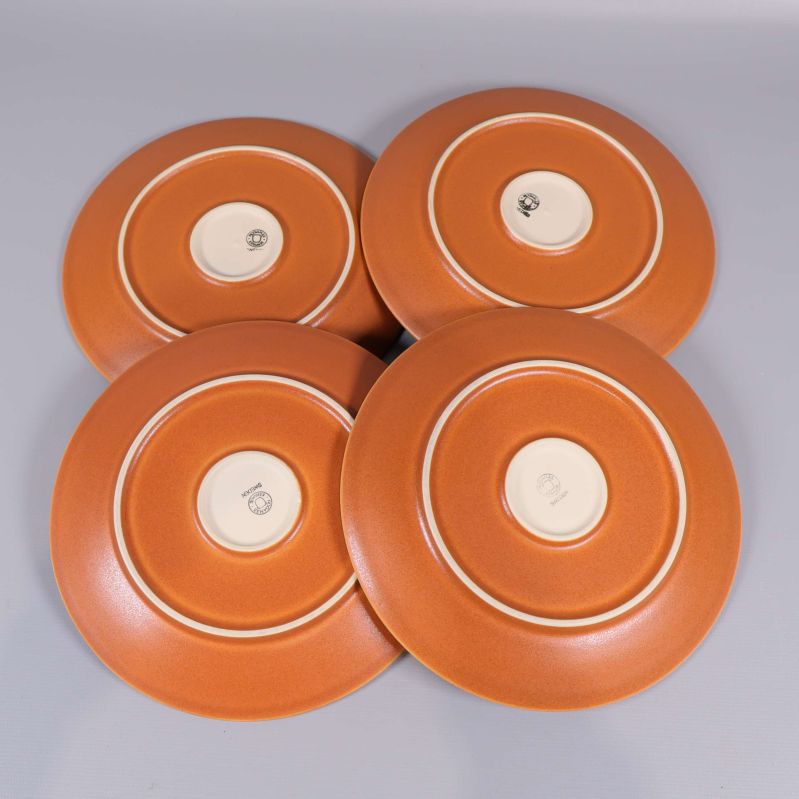 Baksidan av fyra orangea assietter visar keramikens märkning