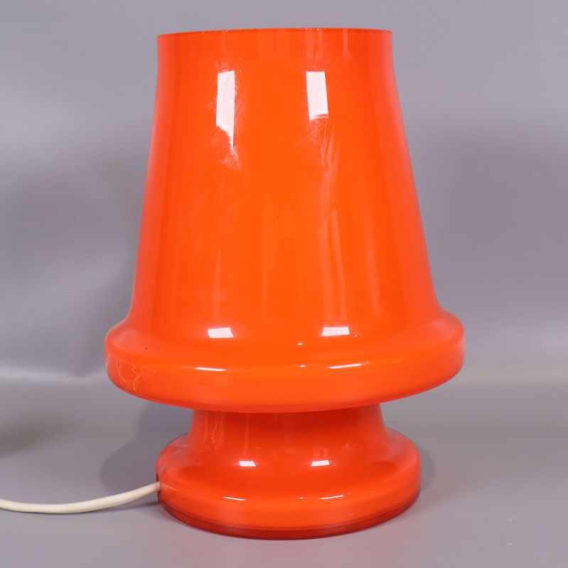 Orange bordslampa i glas fotograferad rakt framifrån