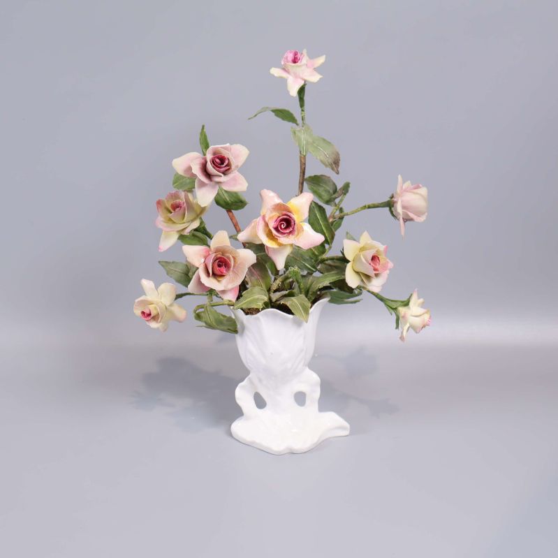Vit porslinsvas med rosa konstblommor på grå bakgrund