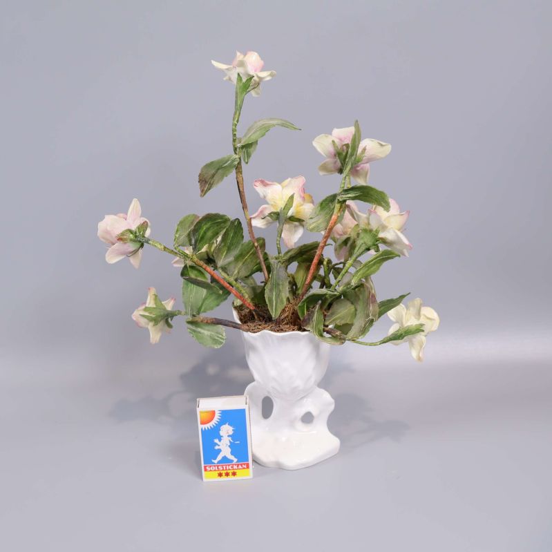 Vas med konstblommor bredvid tändsticksask för storleksjämförelse