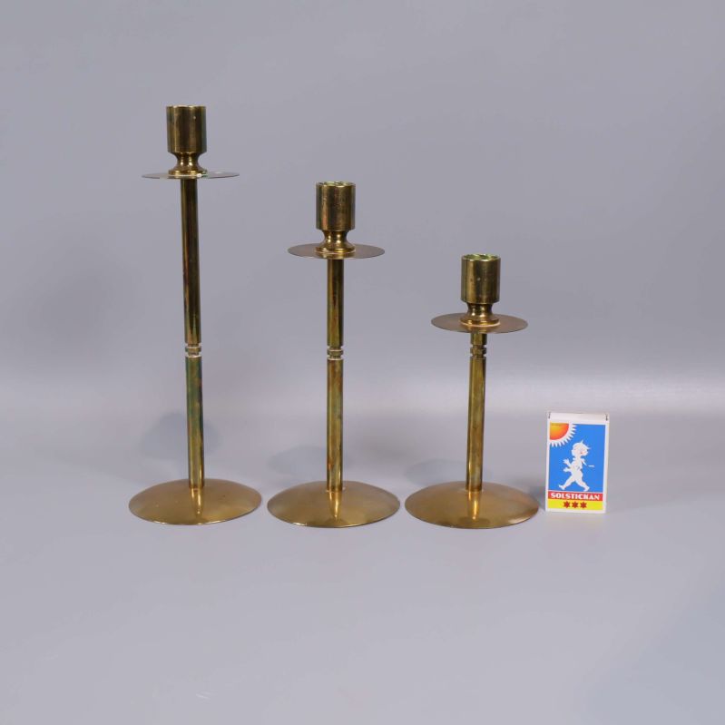 Tre ljusstakar i mässing bredvid en tändsticksask som storleksreferens
