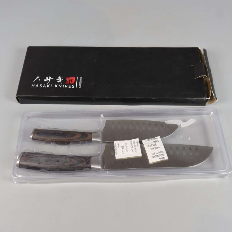 Två köksknivar i plastförpackning bredvid svart ask