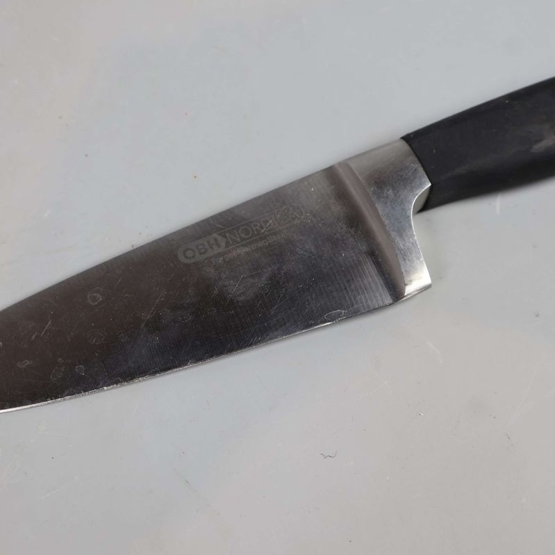 Närbild av kockkniv med svart handtag, text synlig