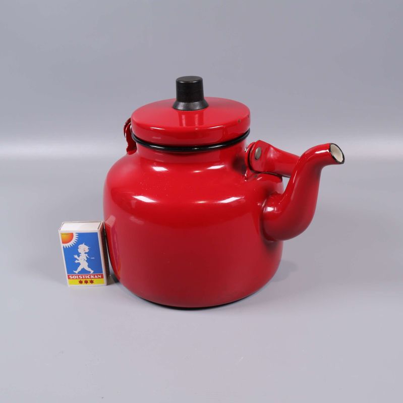 Röd vattenkittel jämte tändsticksask för storleksreferens