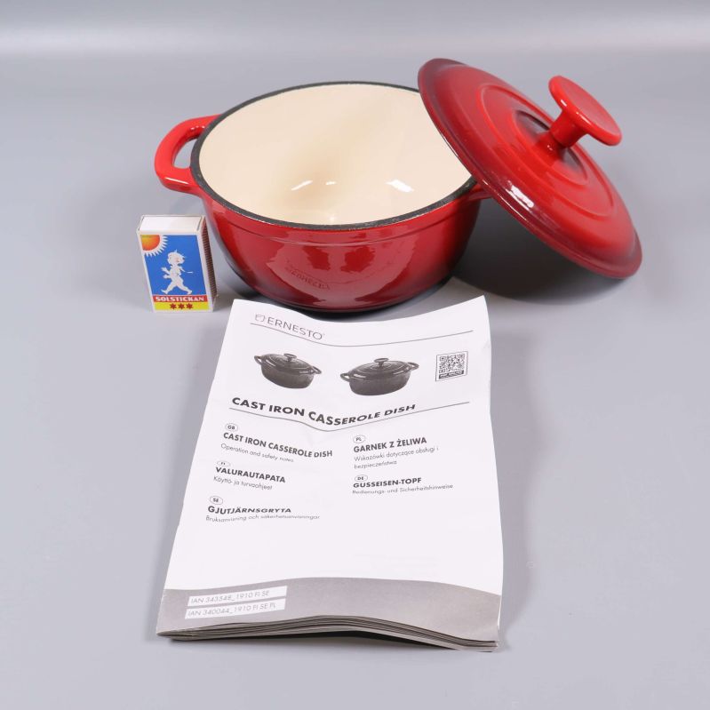 Röd gryta med lock bredvid tändsticksask och manual