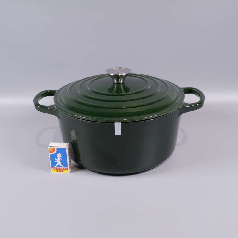 Mörkgrön gjutjärnsgryta med lock bredvid tändsticksask