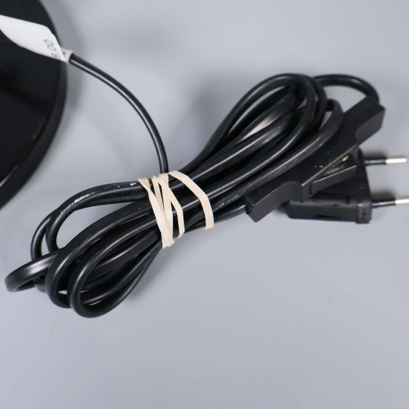 Svart elkabel med kontakt hoprullad vid lampfoten