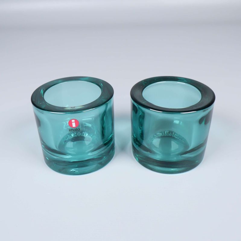 Två turkosa ljuslyktor i glas på vit bakgrund