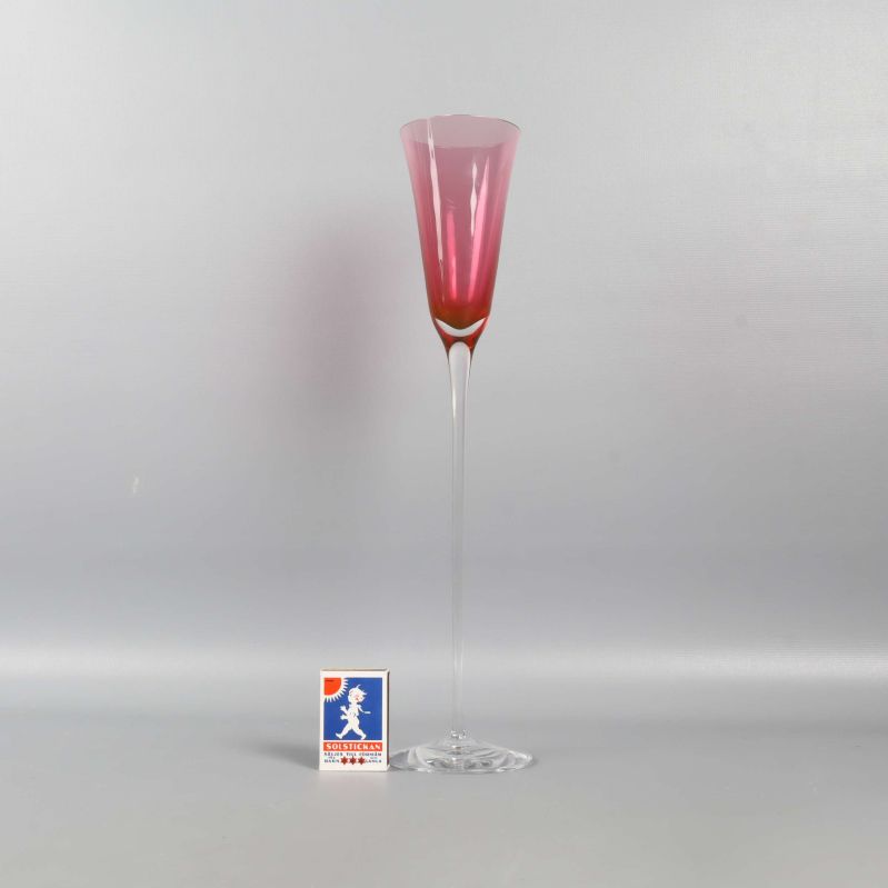 Högt glas med rosa kupa och en tändsticksask bredvid för storleksreferens