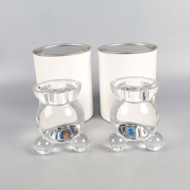 Två runda glasljusstakar framför vita cylindriska förpackningar