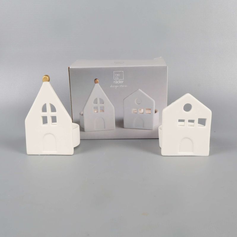 Två vita ljushållare formade som små hus står bredvid en presentförpackning