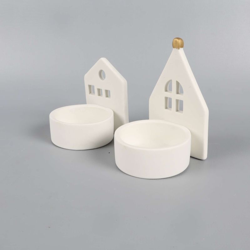 Två vita ljushållare i husform i sned vinkel från sidan