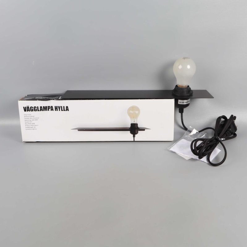 Vägglampa med glödlampa och svart hylla samt förpackning