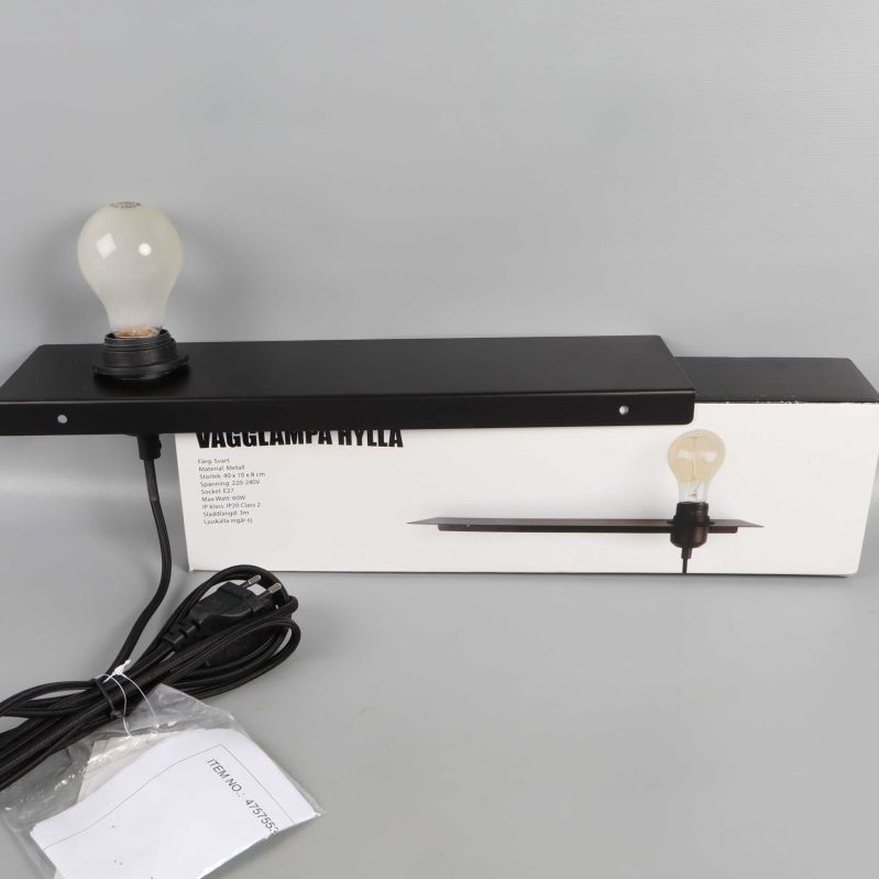 Svart vägglampa med glödlampa och lång sladd ovanpå kartong