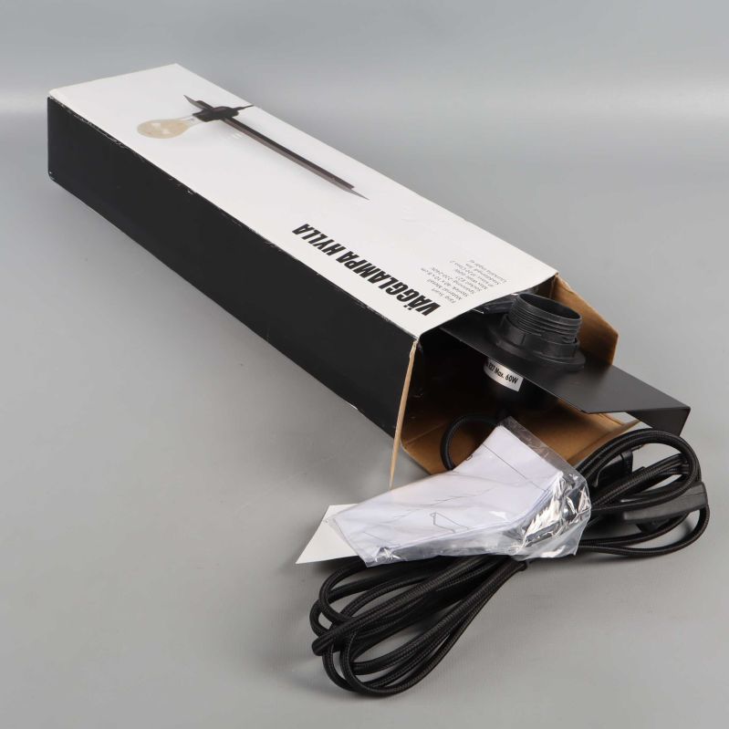 Oöppnad förpackning med svart vägglampa och sladd synlig