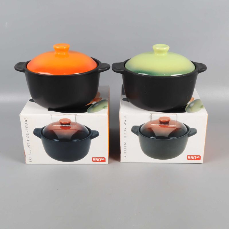 Två svarta grytor med grönt och orange lock stående på kartonger