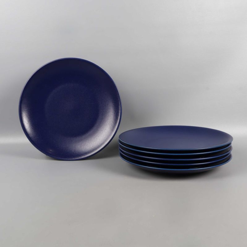 En mörkblå tallrik stående och fem staplade på rad
