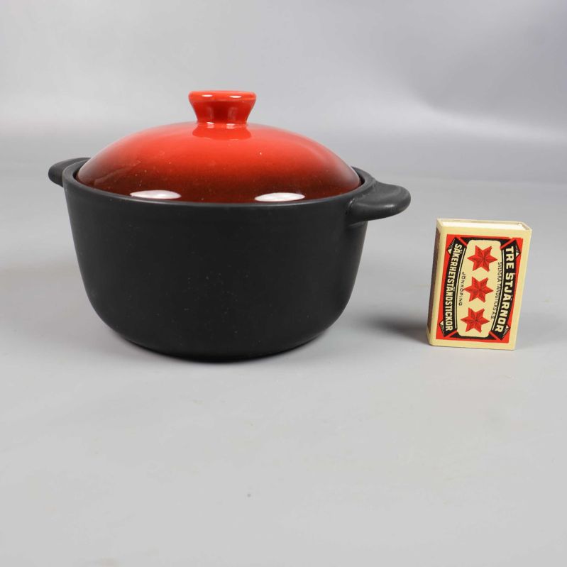 Svart gryta med rött lock bredvid tändsticksask