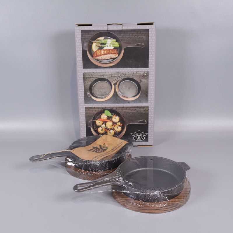 Två portionspannor med träunderlägg och originalkartong i bakgrunden